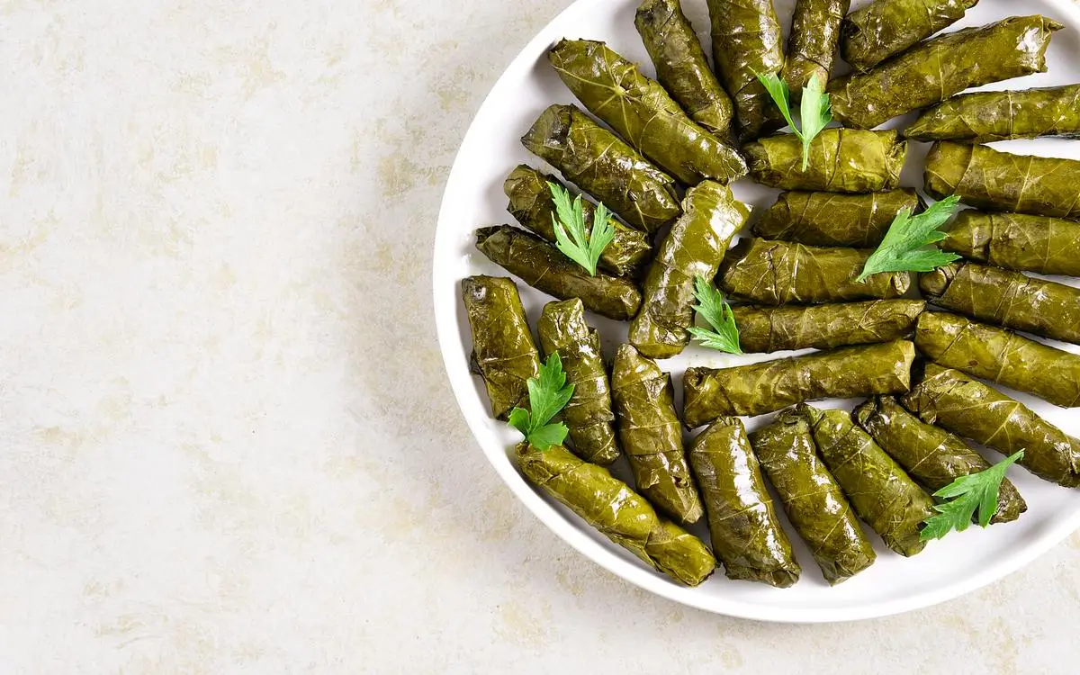 A plate of traditional Mediterranean dolmas, stuffed grape leaves filled with rice and herbs, garnished with fresh parsley.