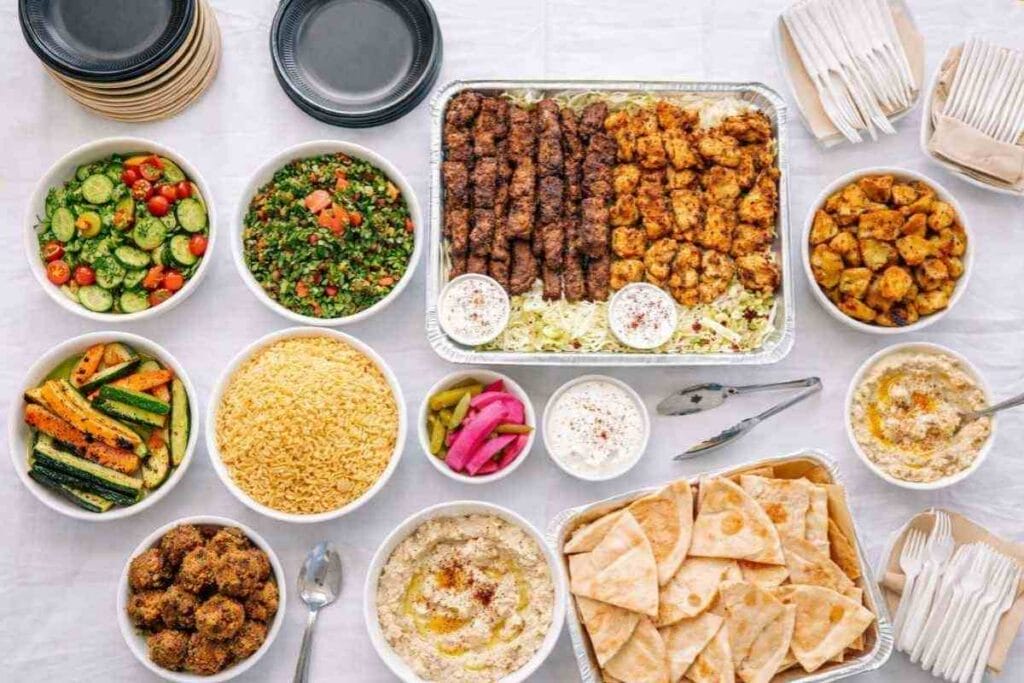 Mediterranean catering Houston spread from Aladdin Mediterranean Cuisine (Aladdin Montrose) with kabobs, tabbouleh, hummus, pita, rice, falafel, salads, grilled veggies, pickles, and sauces.